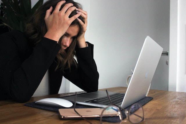 woman with her hands on her head staring at her open laptop